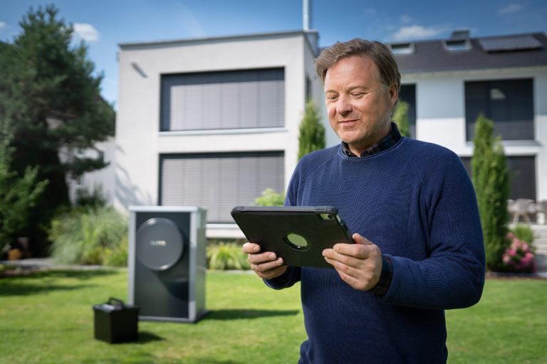 Wärmepumpen Mann mit Tablet steht im Garten neben einem Heizungsgerät und einem modernen Haus.